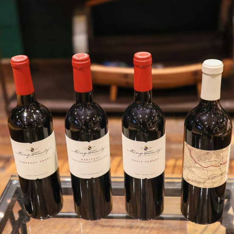 Wine Tasting Experiences Outdoor patio furniture with pink cushions overlooking lush Kelowna's vineyard rows.